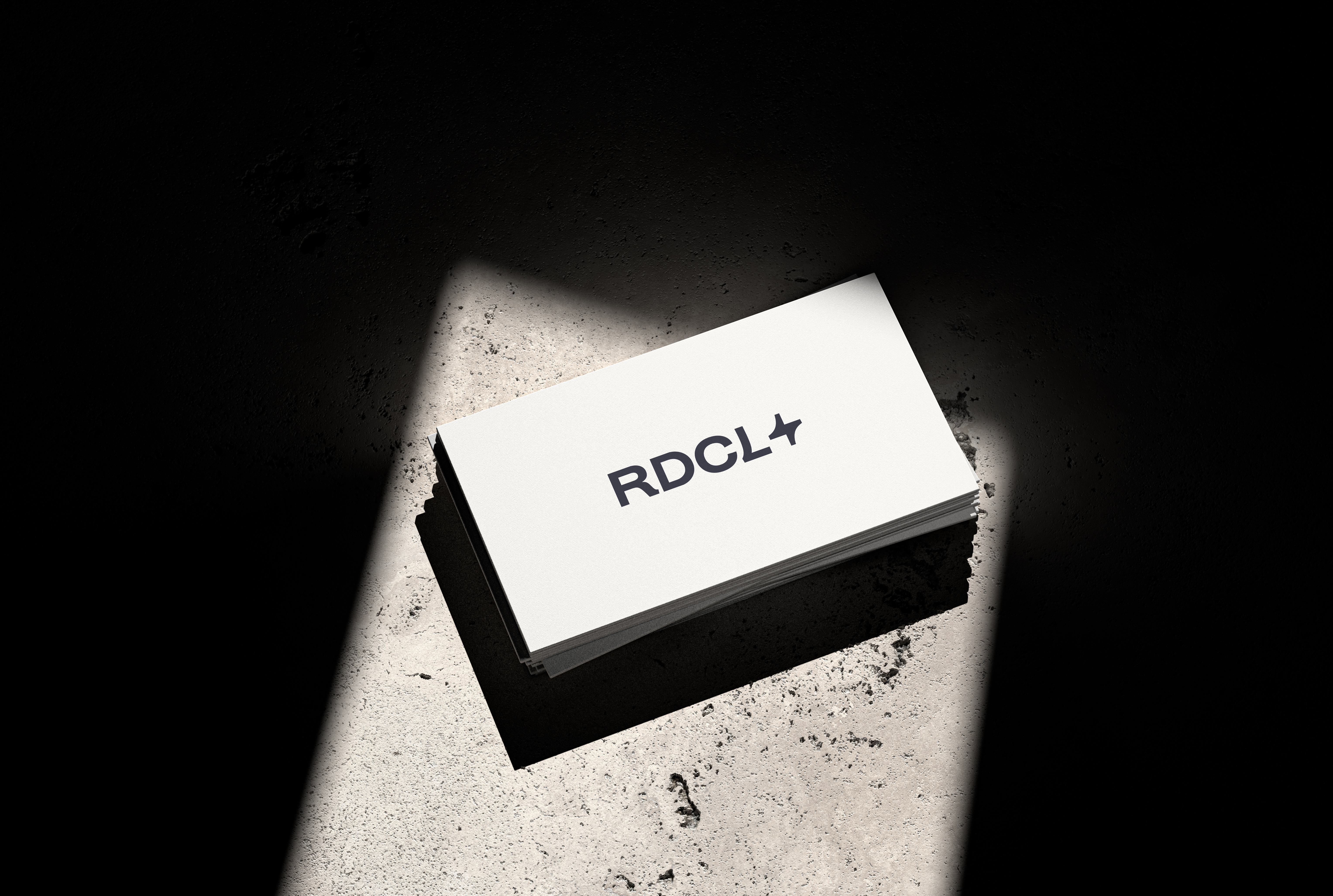 RDCL business cards stacked on textured concrete under dramatic spotlight